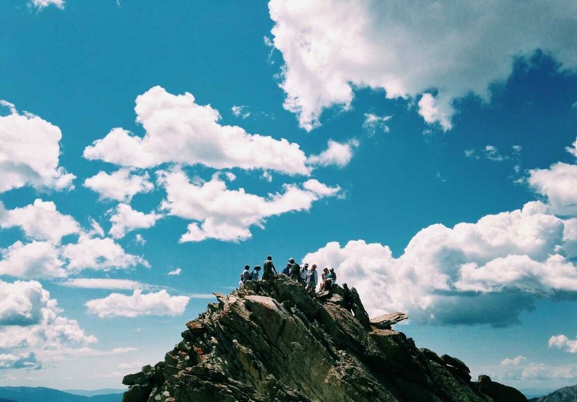 A group of people standing on top of a rocky hill underneath a bright blue sky with white clouds