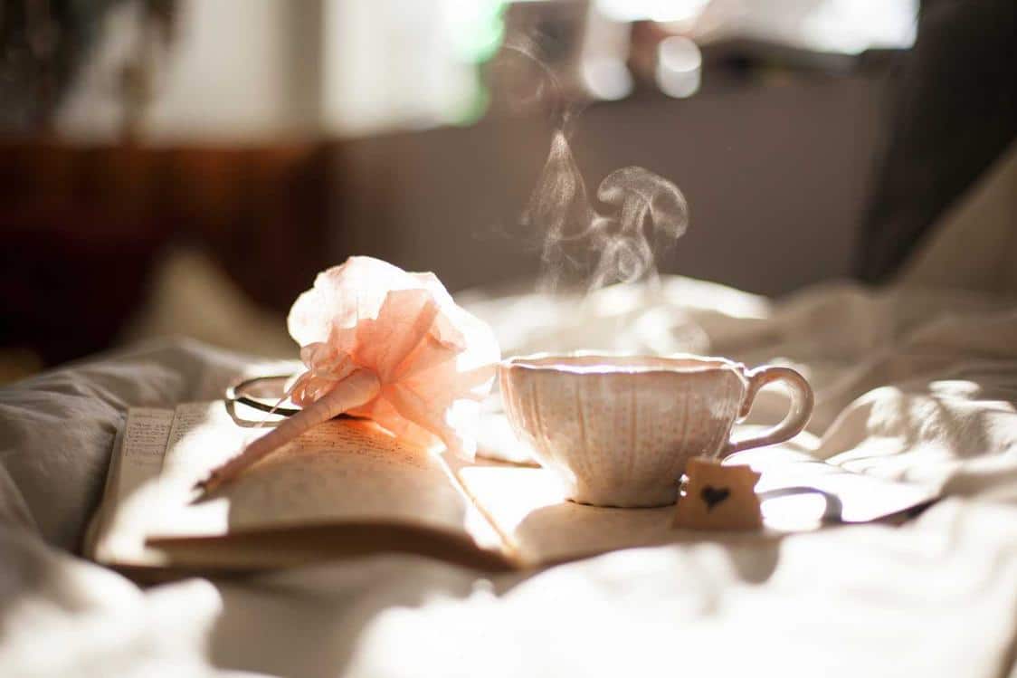 A pen, notepad and mug filled with a steaming hot drink resting on a soft surface