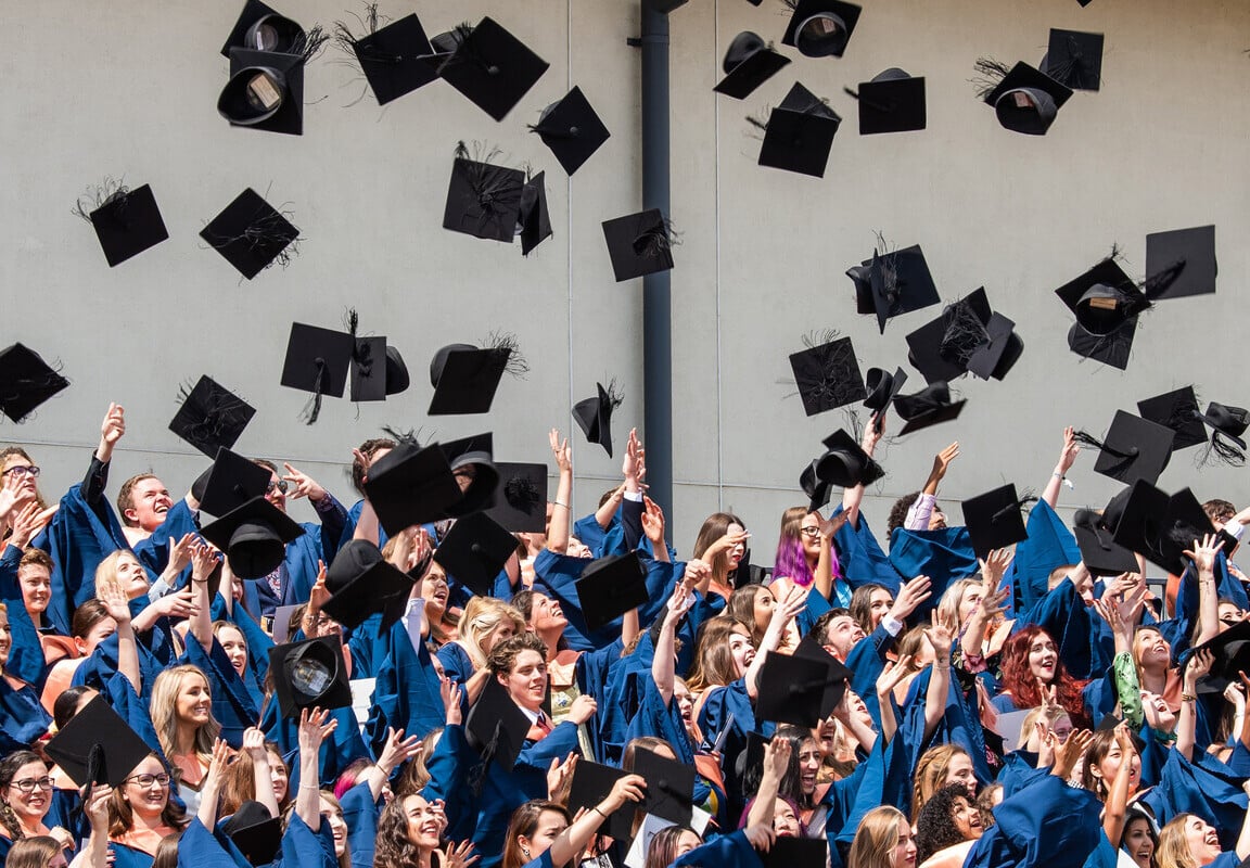 A group of students in graduation robes throwing their mortarboards into the air