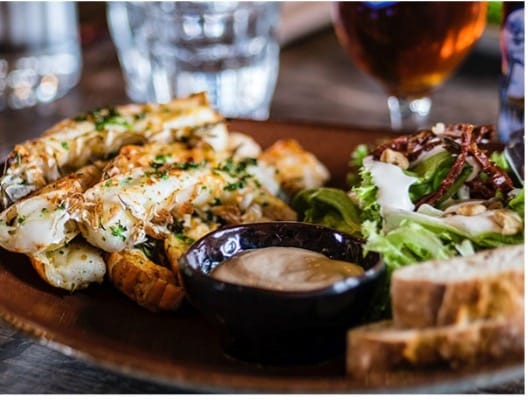 A plate of food on a table with drinks glasses in the background