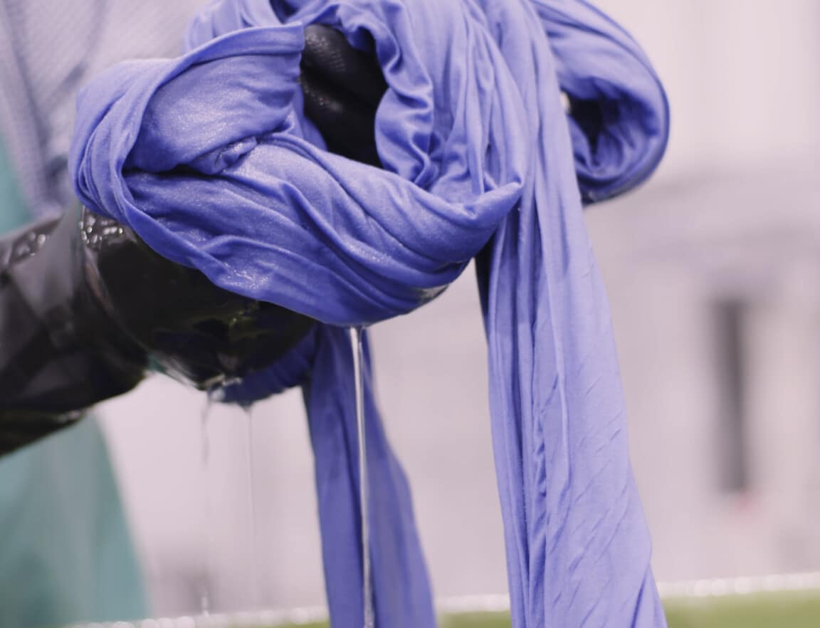 A long piece of purple fabric being dyed by hand