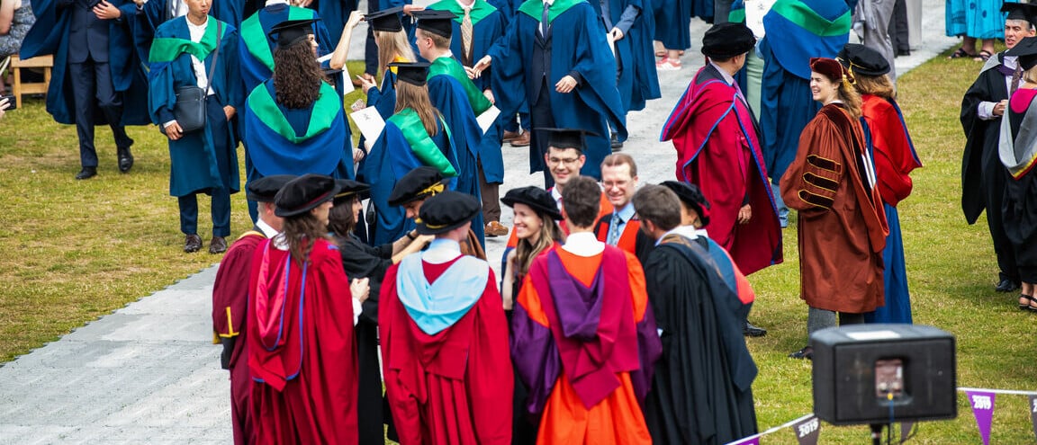 A group of people at a graduation ceremony wearing formal red and orange gowns with black hats