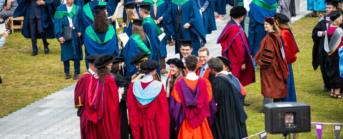 A group of people at a graduation ceremony wearing formal red and orange gowns with black hats