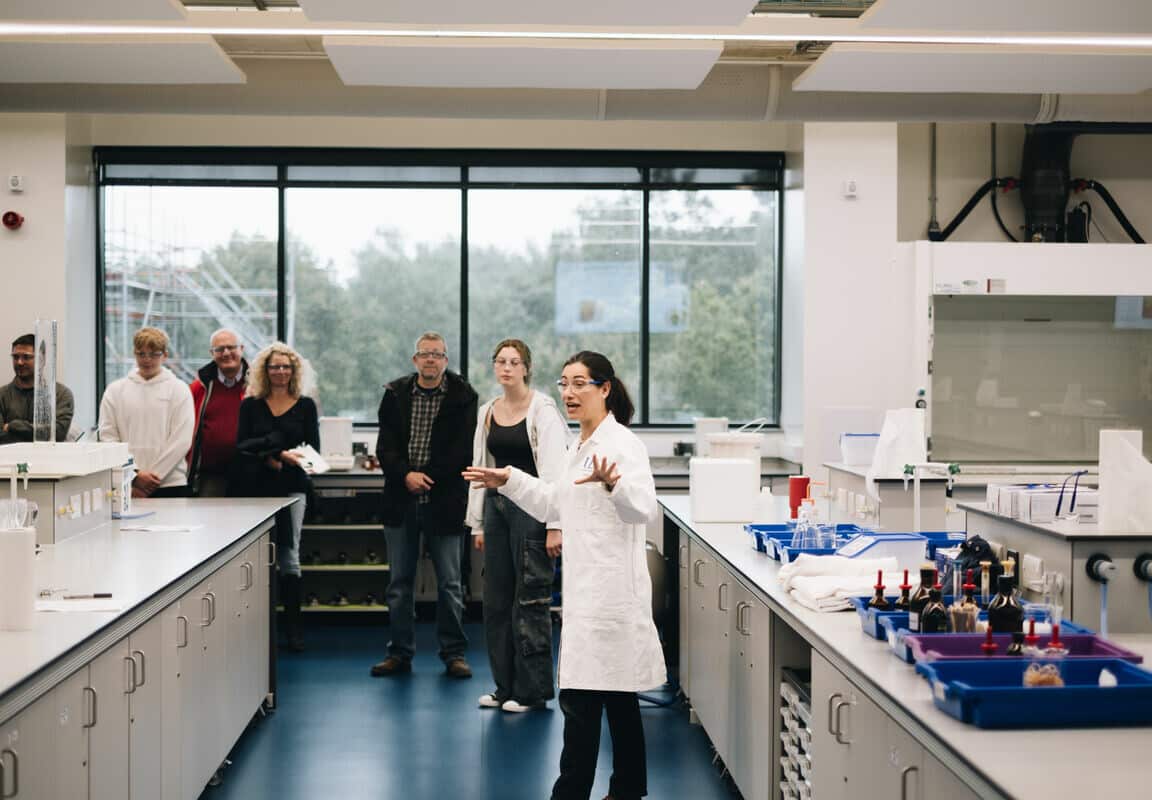 A group of people in a laboratory listening to a lecturer wearing a white lab coat