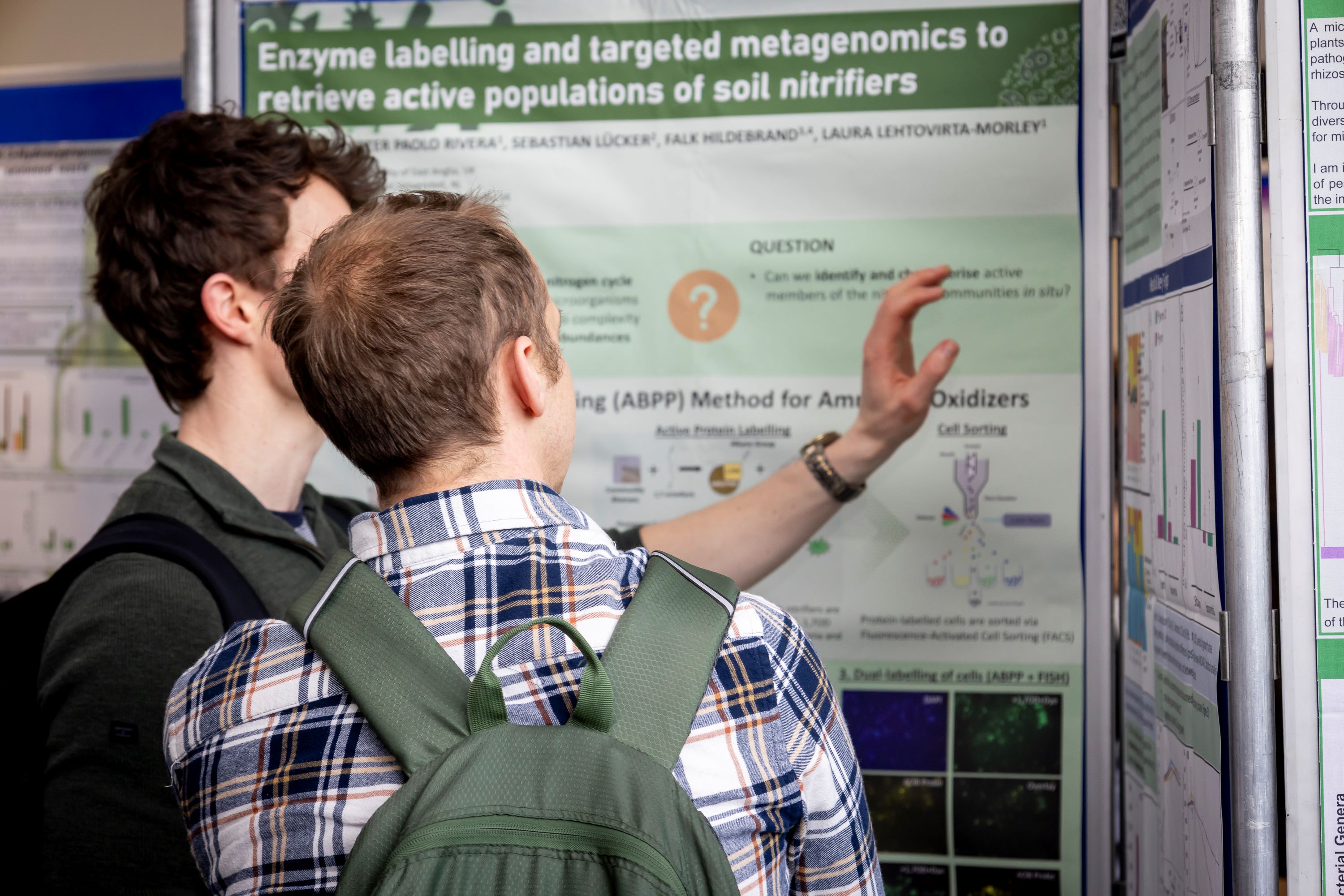 Two scientists discussing a nearby research poster showing text, figures and graphs
