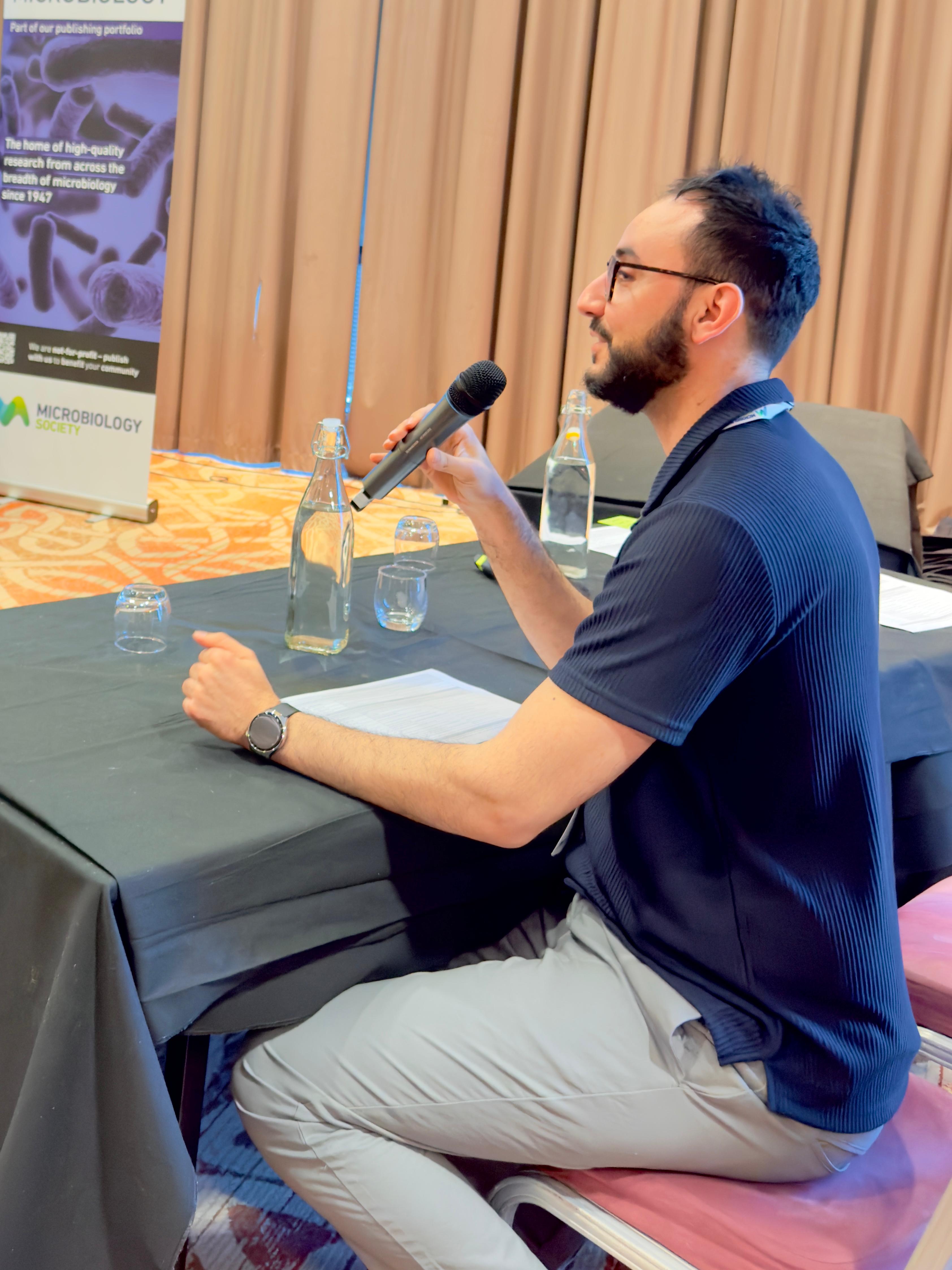Dr Bilal Djeghout holding a microphone to chair a session at the Biofilms 11 conference