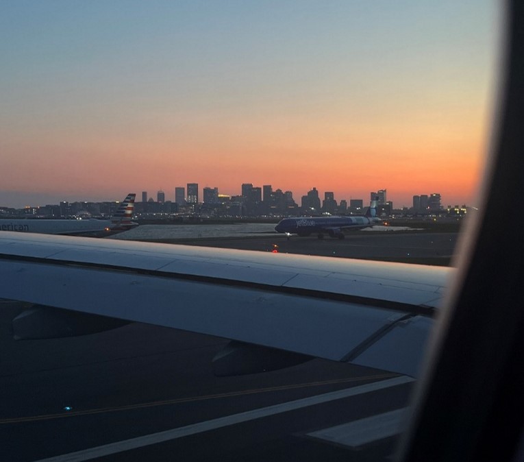 View from a place window looking over the wing with tall city buildings in the distance at sunset
