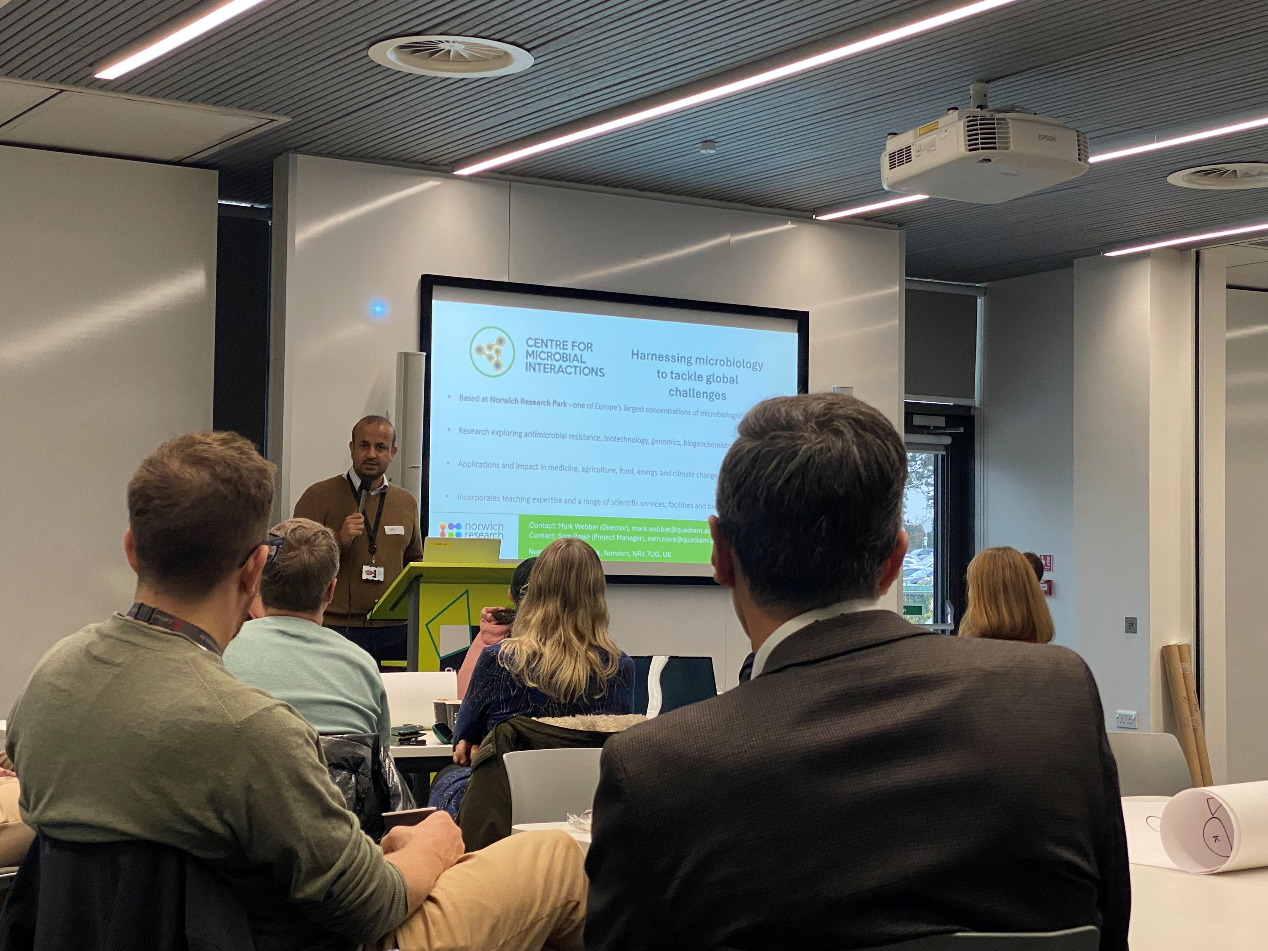 Muhammad Yasir standing in front of a large presentation screen and welcoming attendees to the functional multi-omics symposium