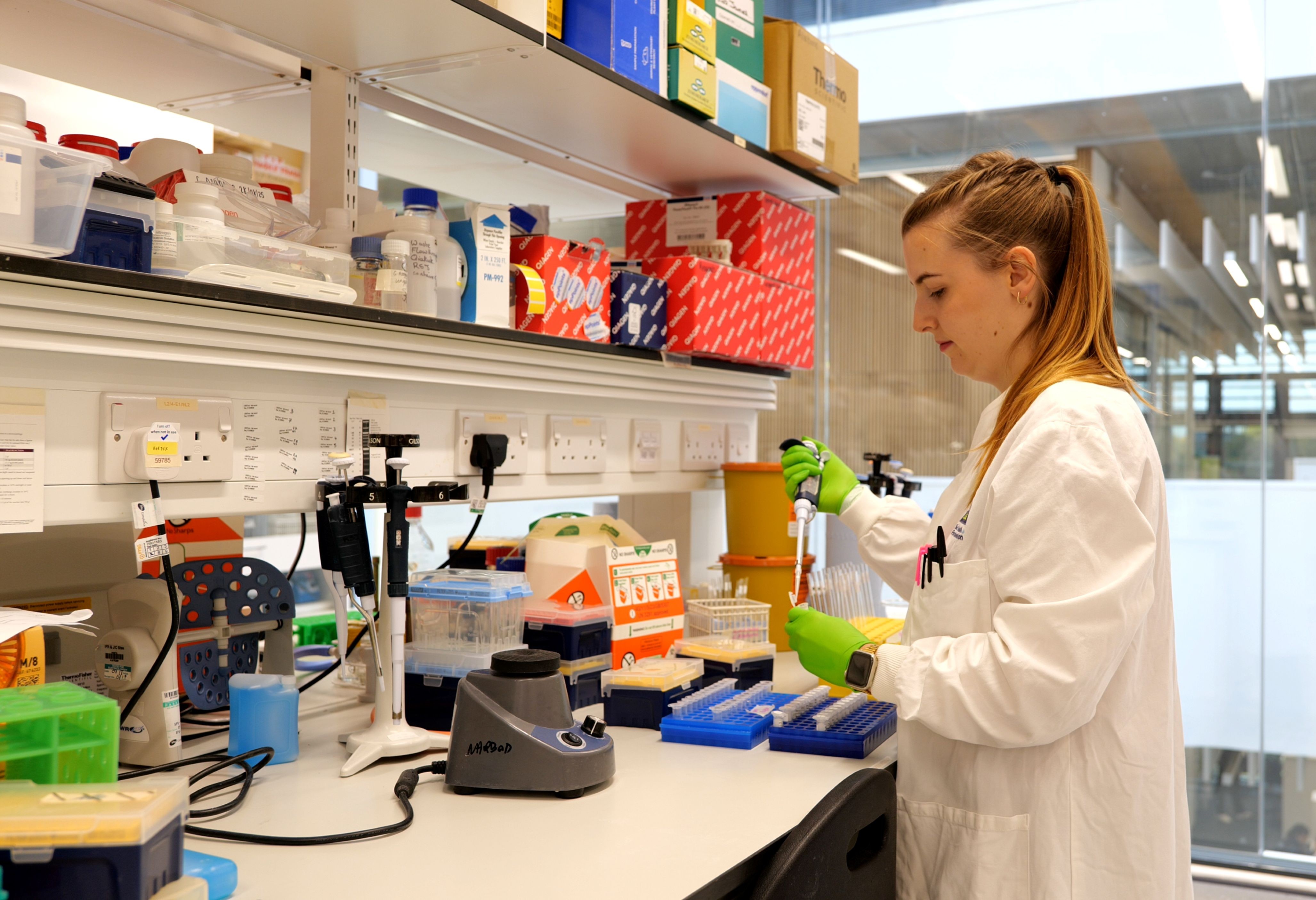 A PhD student working in a laboratory, wearing a white lab coat and holding a pipette.