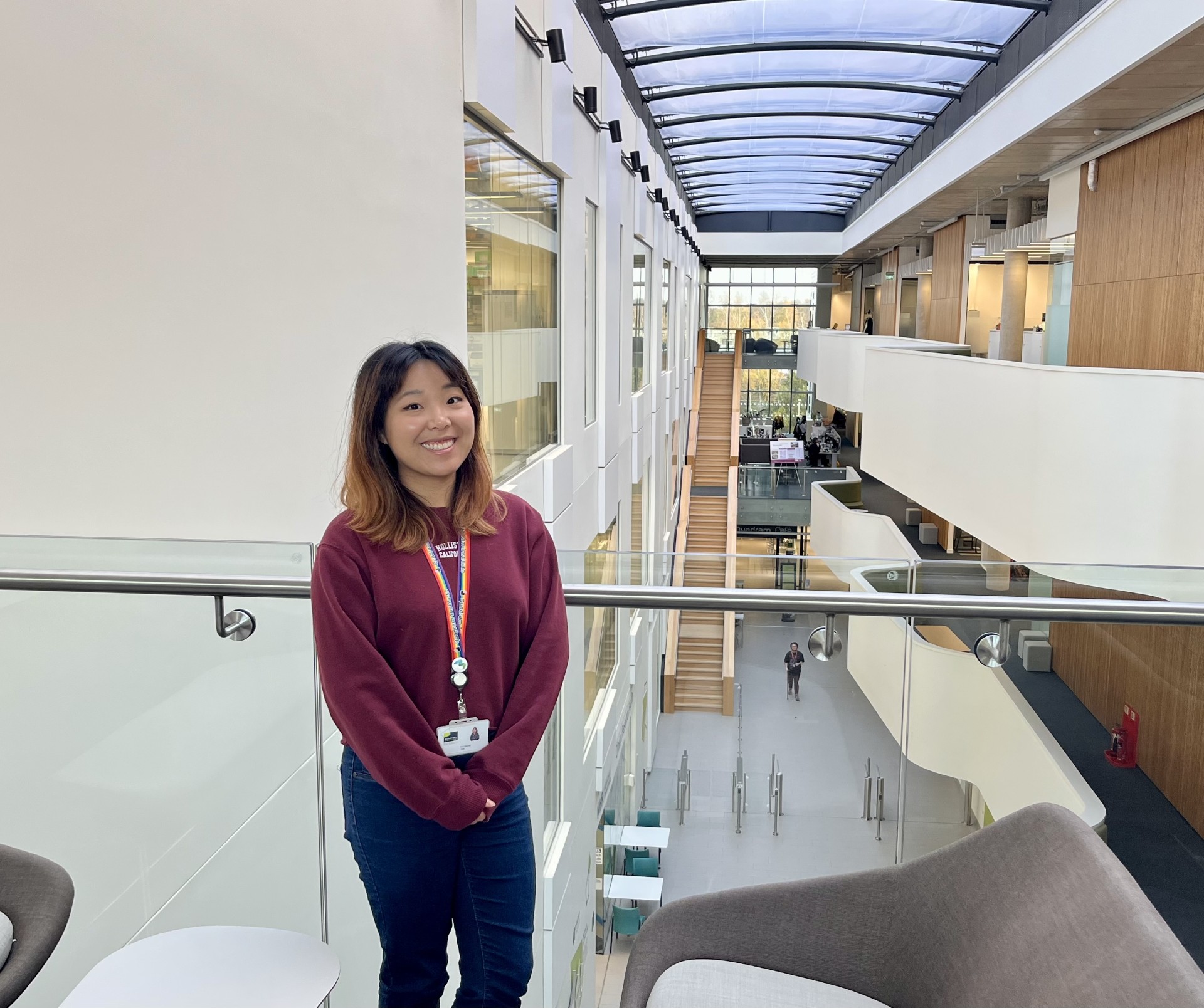 Ka Cheung standing against a glass balcony above the large open space atrium of the Quadram Institute.