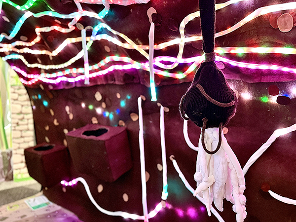 A microbe with brown head and white body hanging in a tunnel of brown threaded with brightly coloured lights