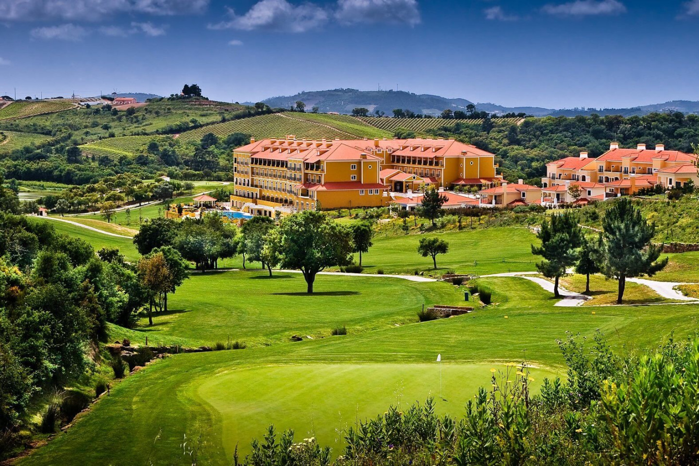 Large conference centre building surrounded by green hills and fields on a sunny day.