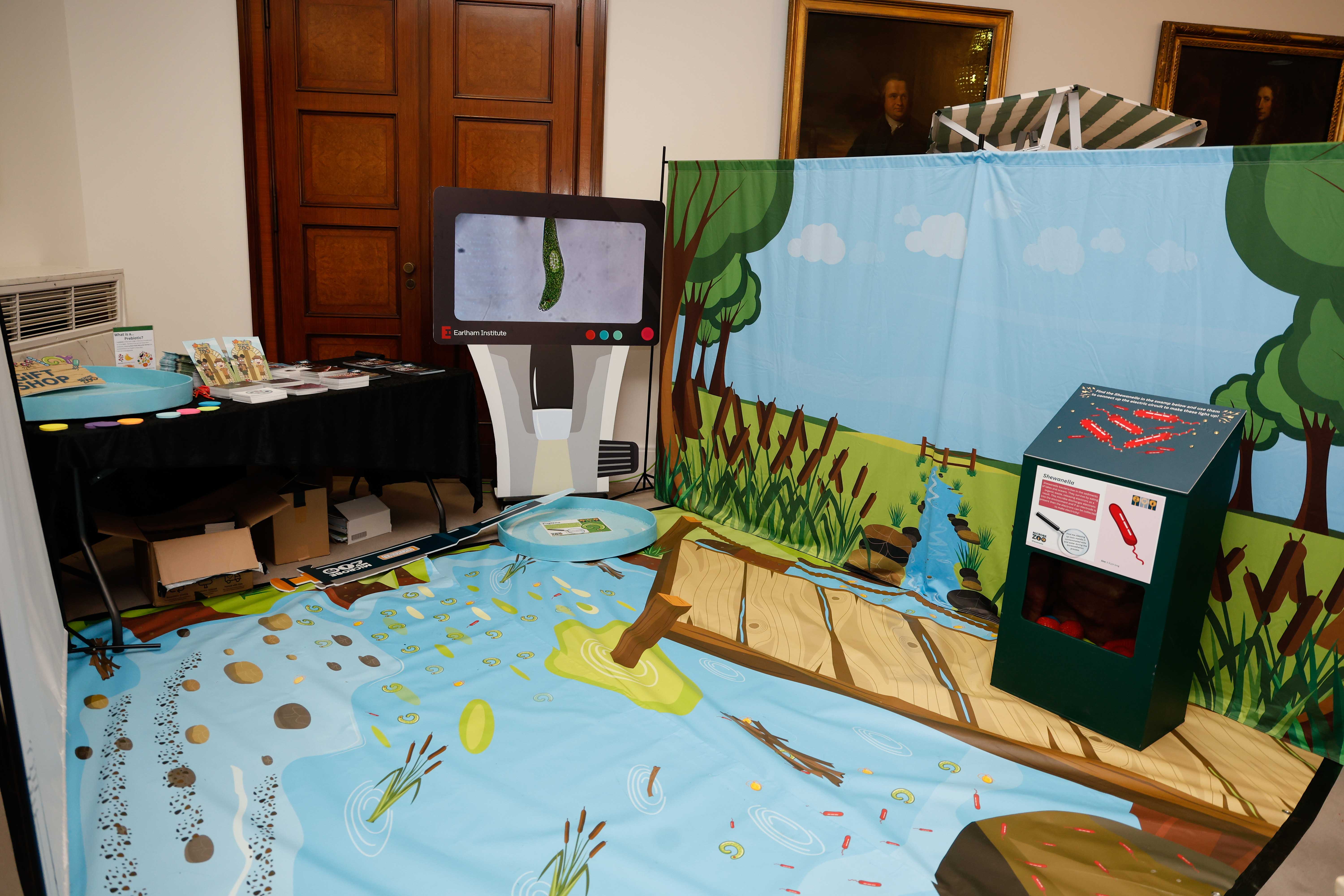 The water zone of the Microbe Zoo exhibit with light blue river graphics on the floor and a countryside graphic in the background showing the different microbes found in these ecosystems