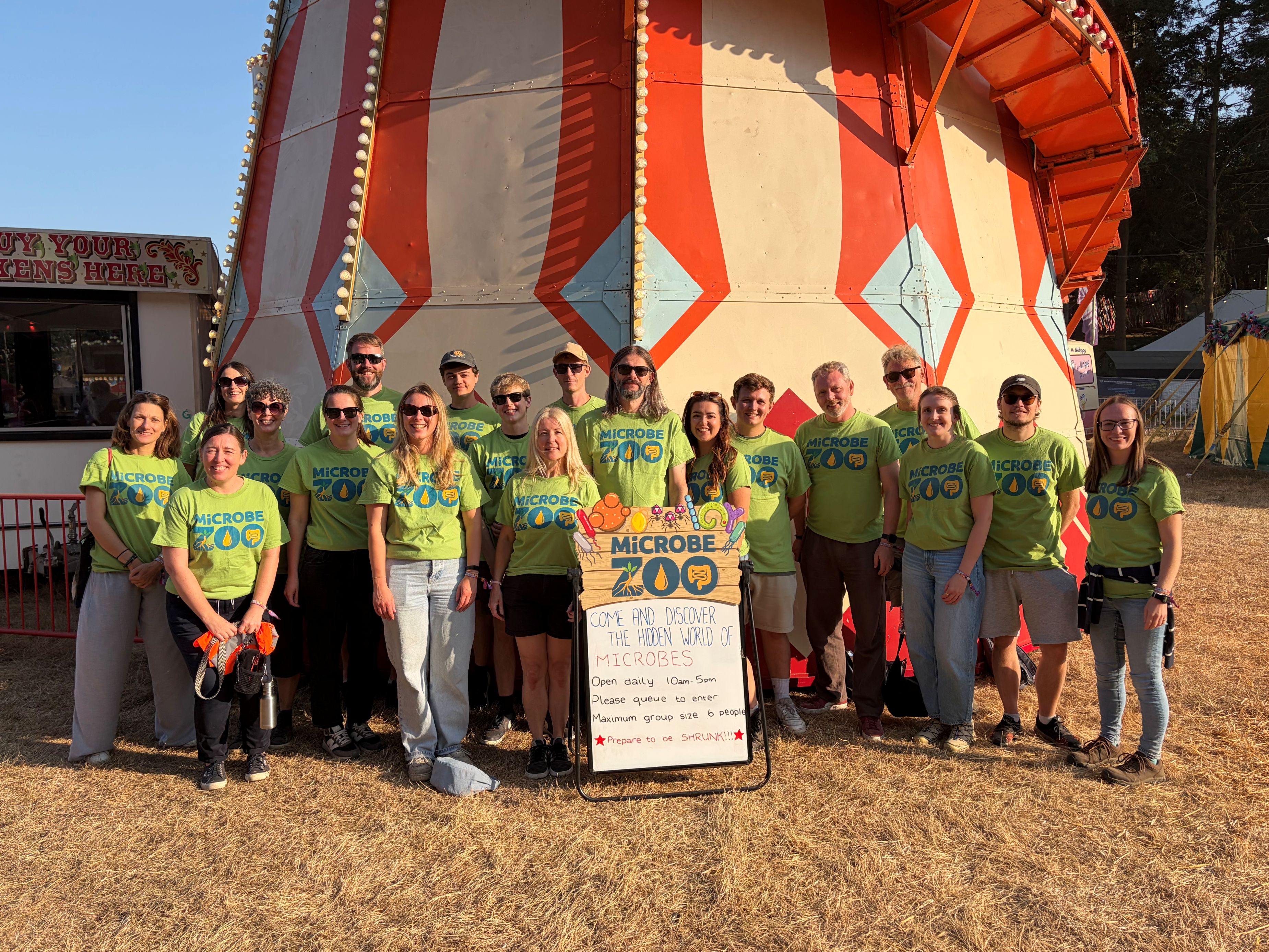Large team of Microbe Zoo volunteers standing in front of a helter skelter ride and wearing bright green branded t-shirts